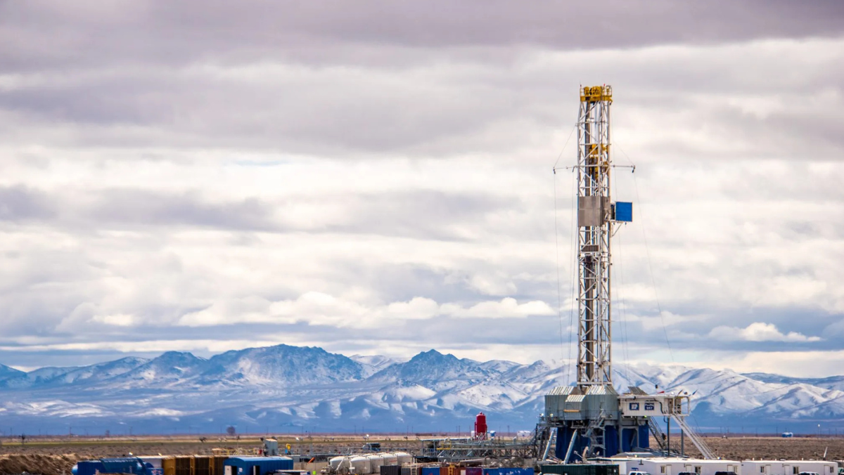 Geothermal drilling rig operating in a wide desert landscape with snowy mountains in the background