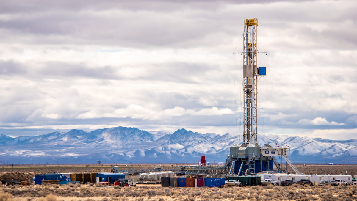 Geothermal drilling rig operating in a desert landscape with snow-covered mountains in the distance.