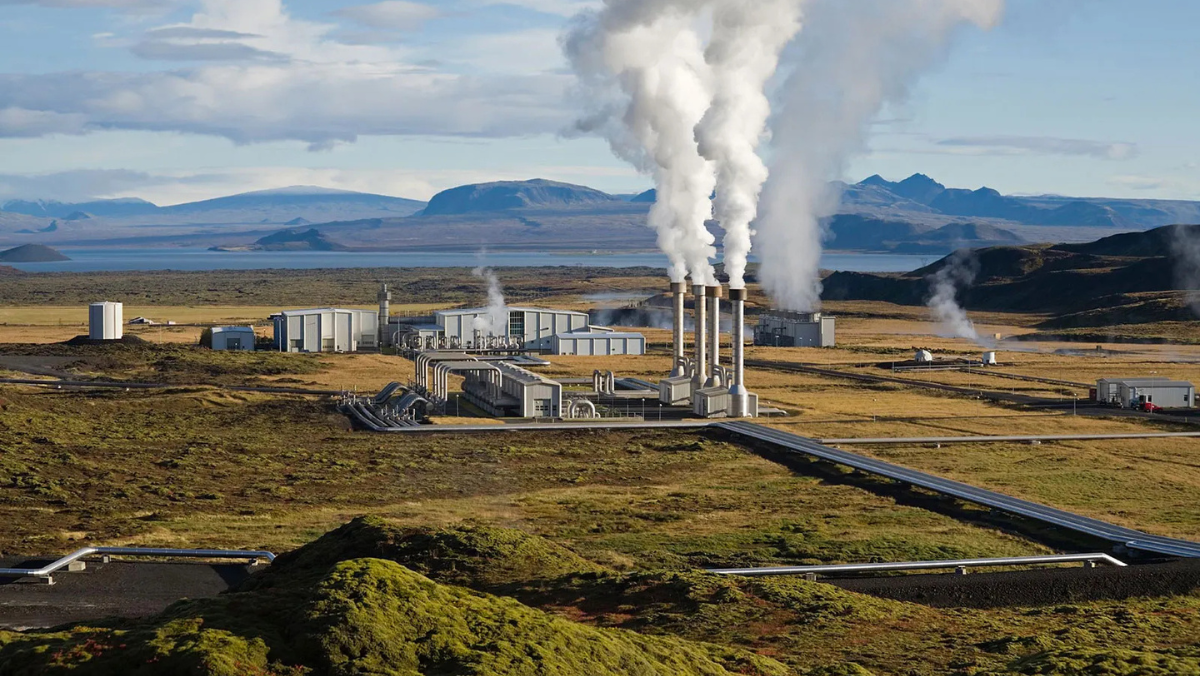 Geothermal power plant with steam rising from wells across a wide volcanic landscape.