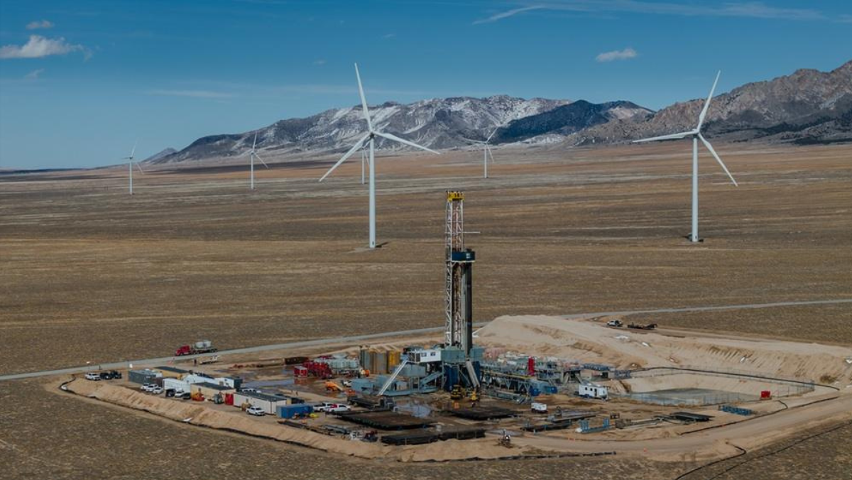Geothermal drilling site with wind turbines in a wide desert landscape.