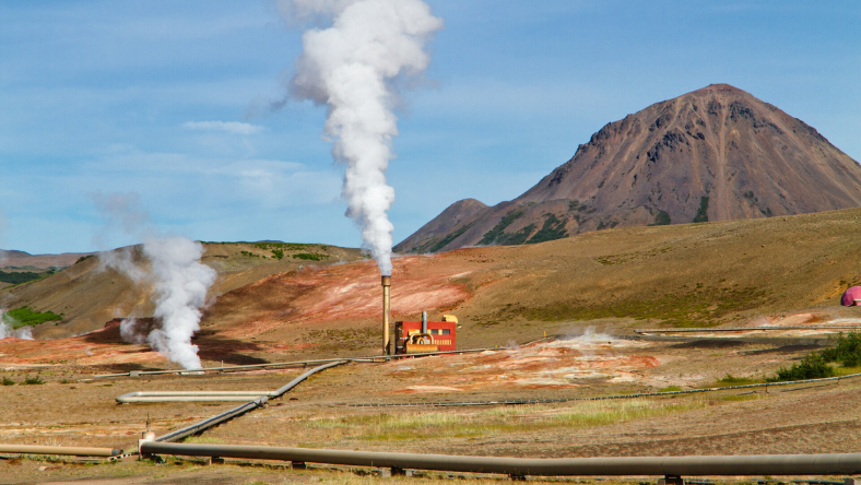 Geothermal power plant with steam rising from wells in a mountainous landscape
