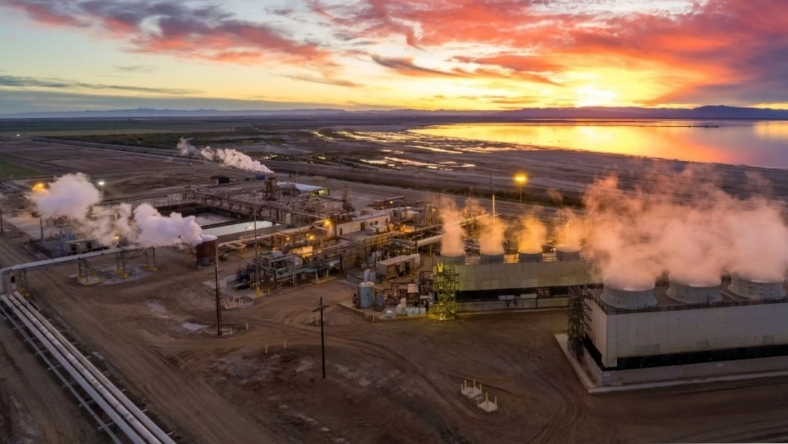 Geothermal power plant with steam rising from cooling units near water at sunset