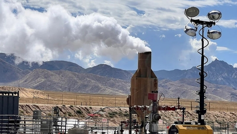 Geothermal test facility with steam venting against mountain backdrop