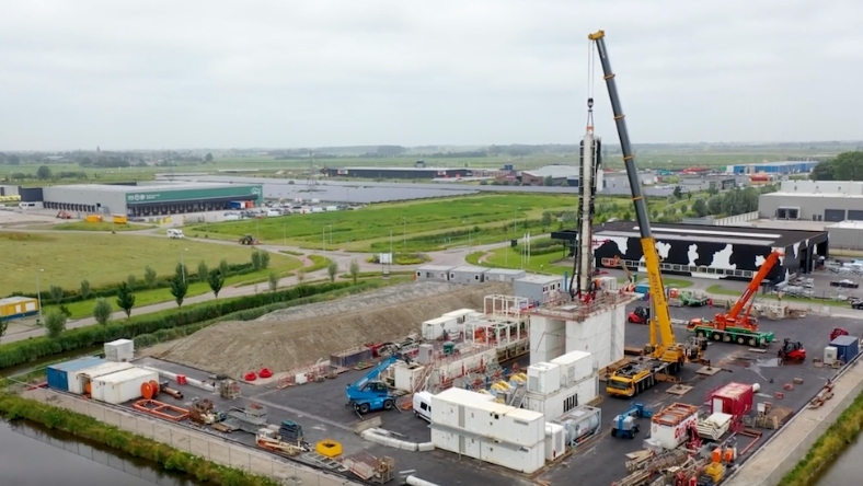 Geothermal well installation site with drilling rig and crane